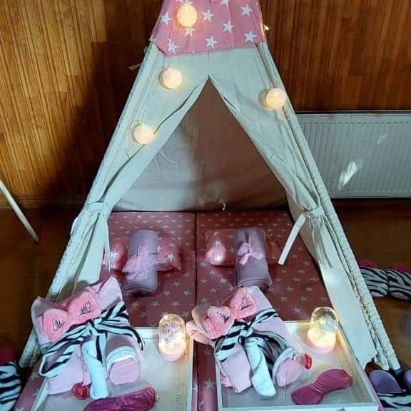 Tipi decorado con estrellas rosadas, guirnalda de luces y kits de pijamada para dos niñas