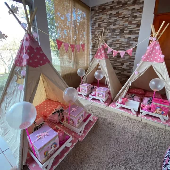 Tres carpas tipi rosadas con estrellas, banderines, globos transparentes y cajas de regalo de unicornio en cada colchoneta